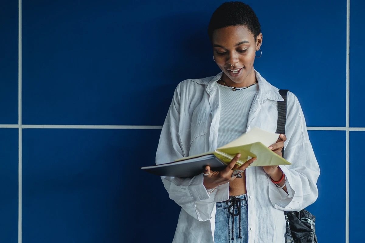Student leaning against blue wall reading a book