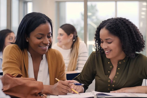 Two people are smiling and studying together at a table in a classroom.